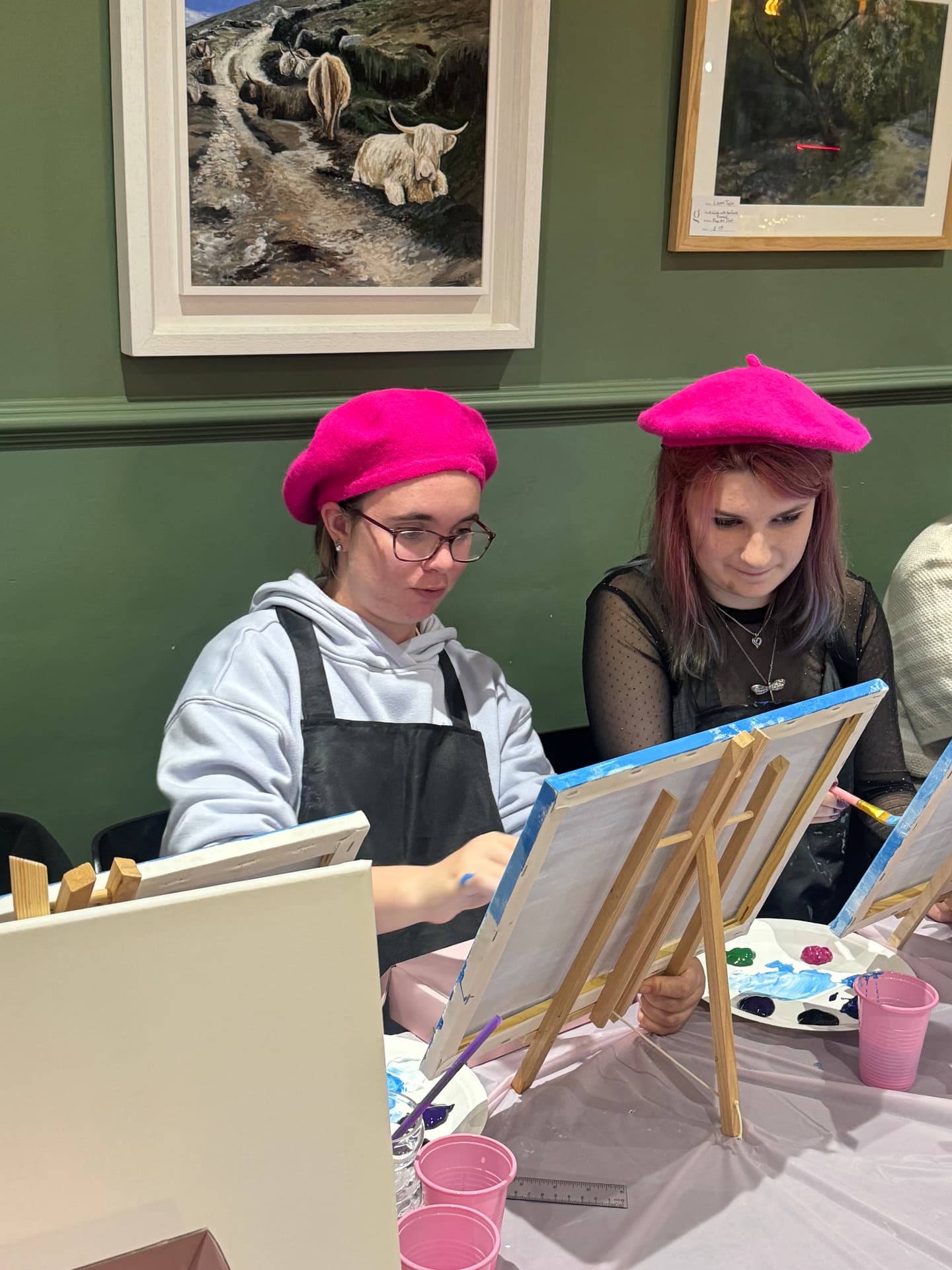 Two young women in pink berets painting side by side at the Newry social group.