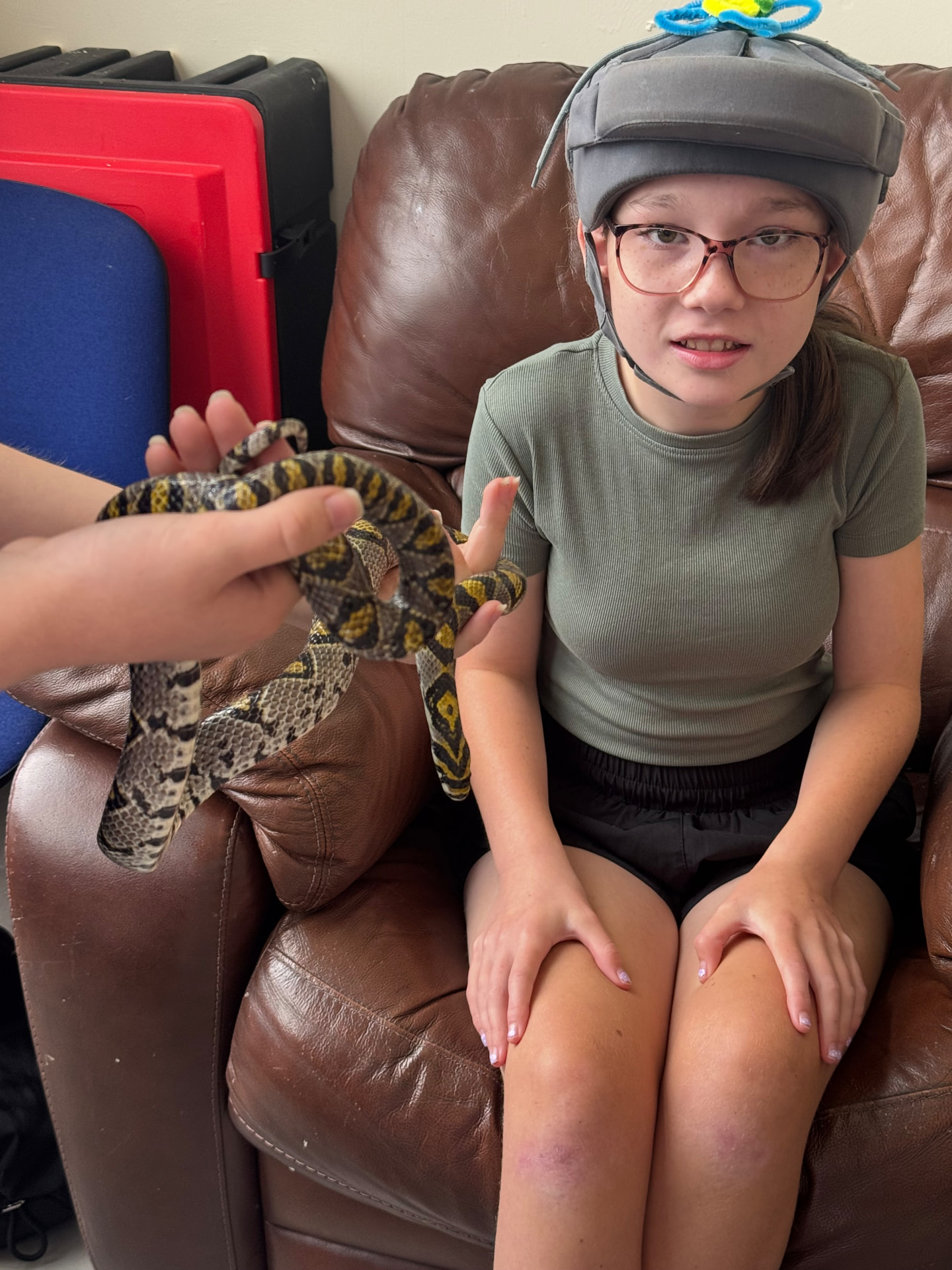 A girl wearing a soft helmet holding a snake with a handler at the ASD Ireland summer camp.