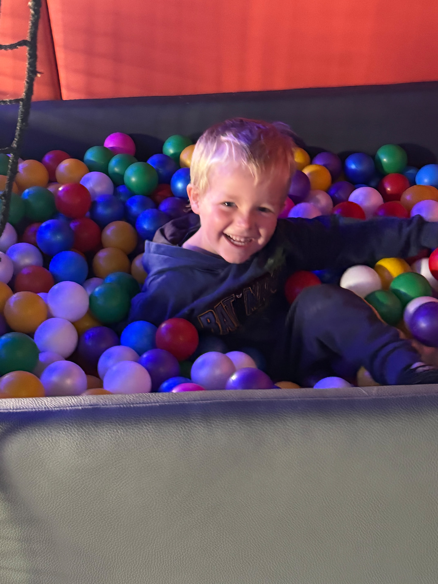 A smiling child sitting in a colourful ball pit inside the mobile sensory room.