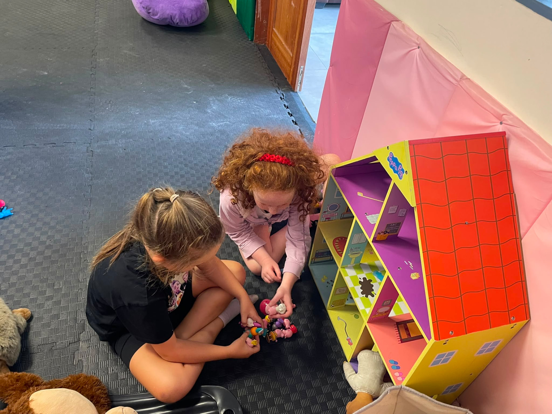 Two girls playing with a colourful dollhouse on soft flooring at the ASD Ireland summer camp.