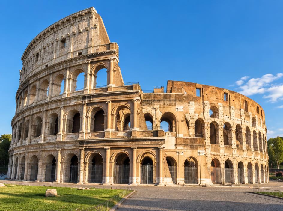 The Roman Colosseum in warm sunshine under a blue sky.