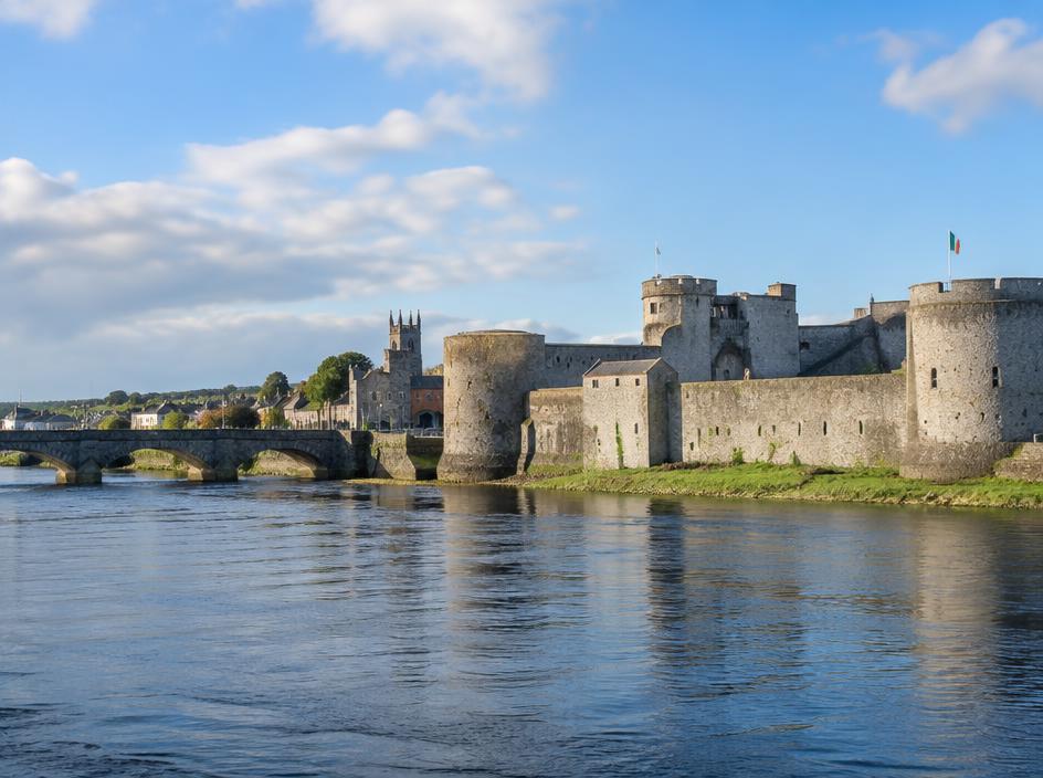 A stone castle with round towers beside a wide river in Limerick.